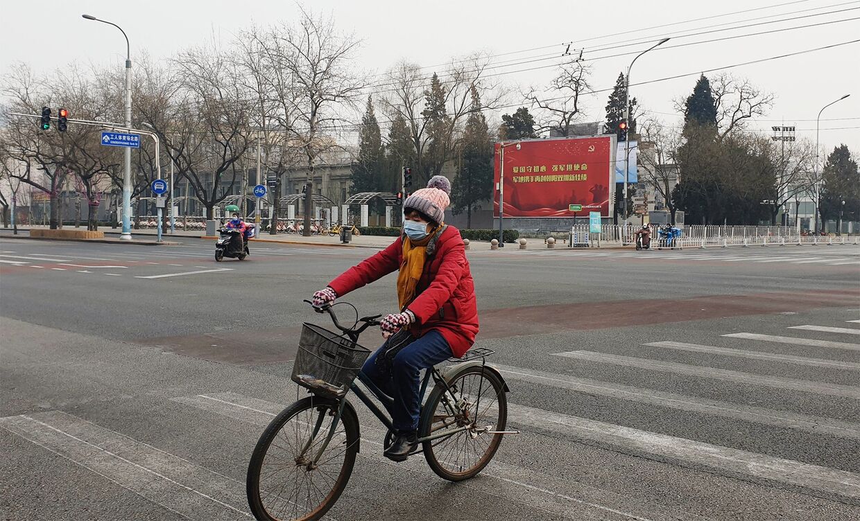 Девушка в медицинской маске едет на велосипеде по улице Пекина