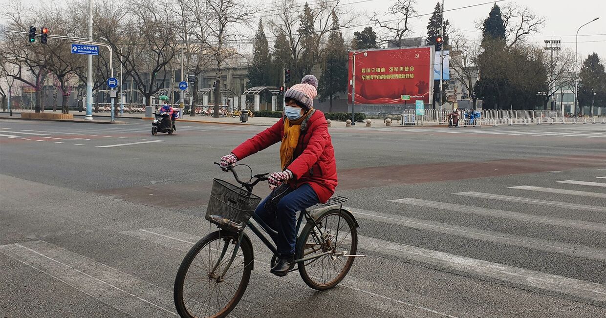 Девушка в медицинской маске едет на велосипеде по улице Пекина