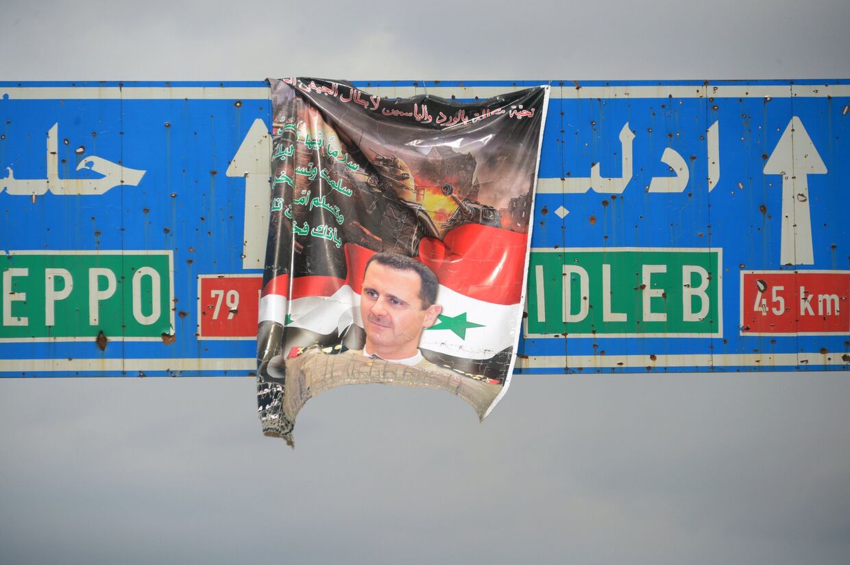 Плакат с портретом президента Сирии Башара Асада на дорожном указателе на город Идлиб в Сирии