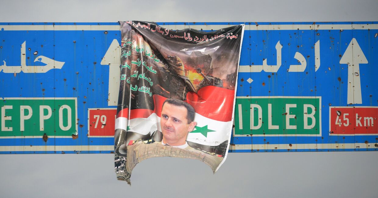 Плакат с портретом президента Сирии Башара Асада на дорожном указателе на город Идлиб в Сирии