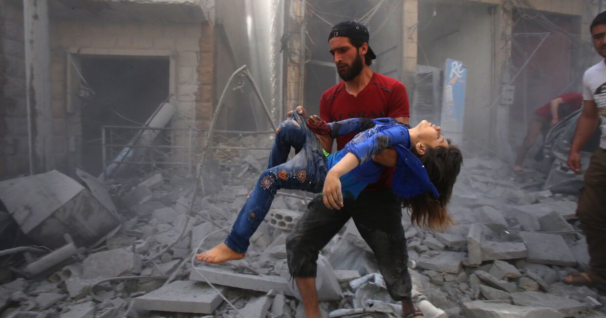 Мужчина несет на руках девочку, пострадавшую при бомбардировке города Маарет ан-Нуман, Сирия