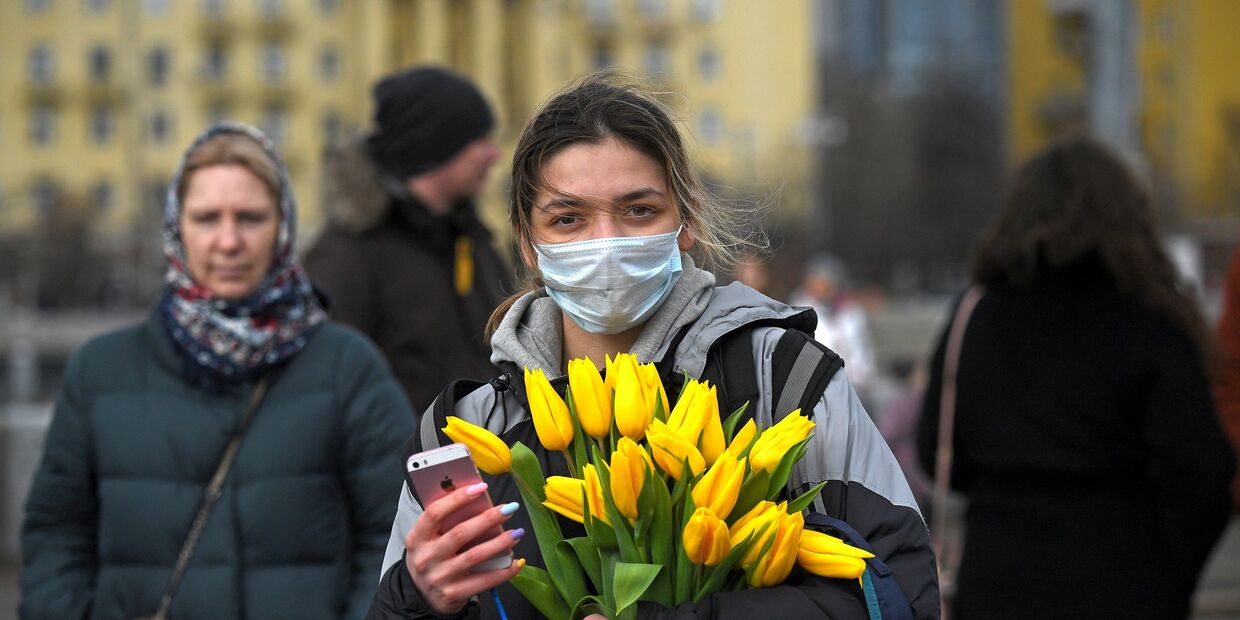 Девушка с цветами и в маске на Пушкинской набережной в Парке Горького в Международный женский день в Москве