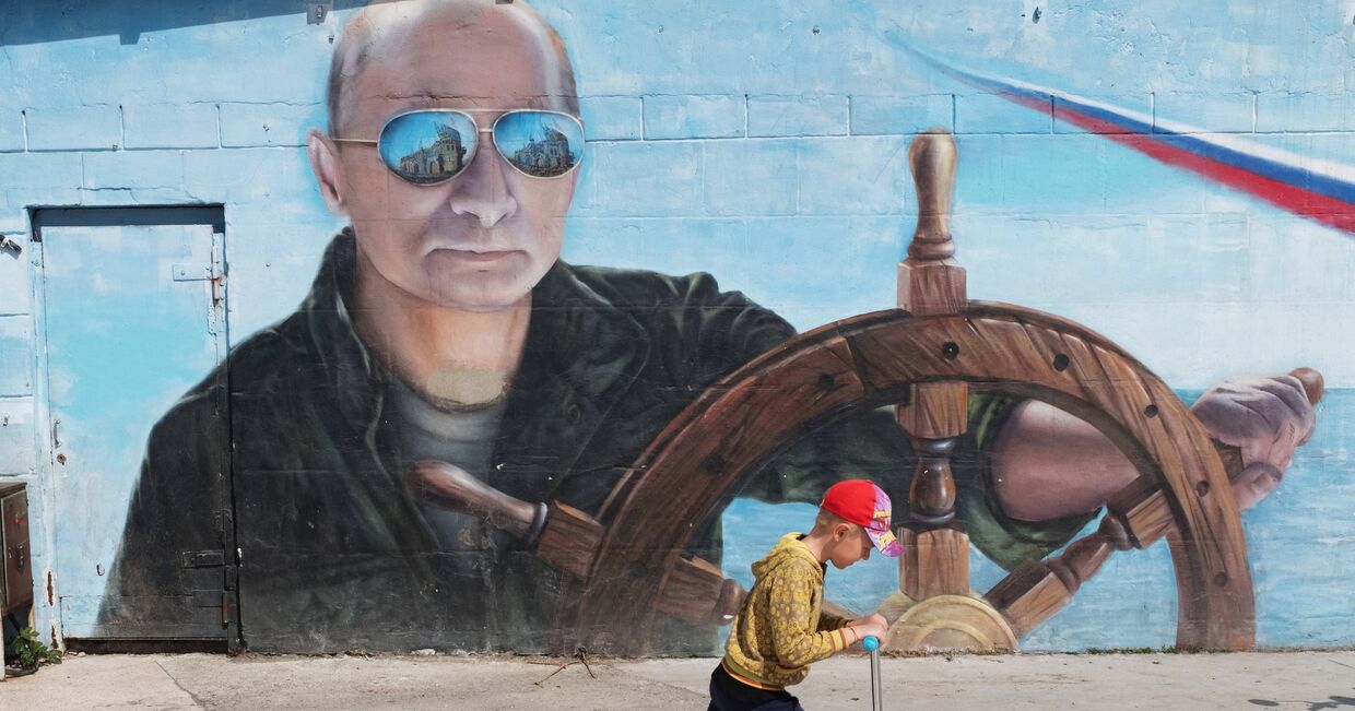 Мальчик проезжает на самокате рядом с граффити с изображением президента РФ Владимира Путина на набережной Ялты