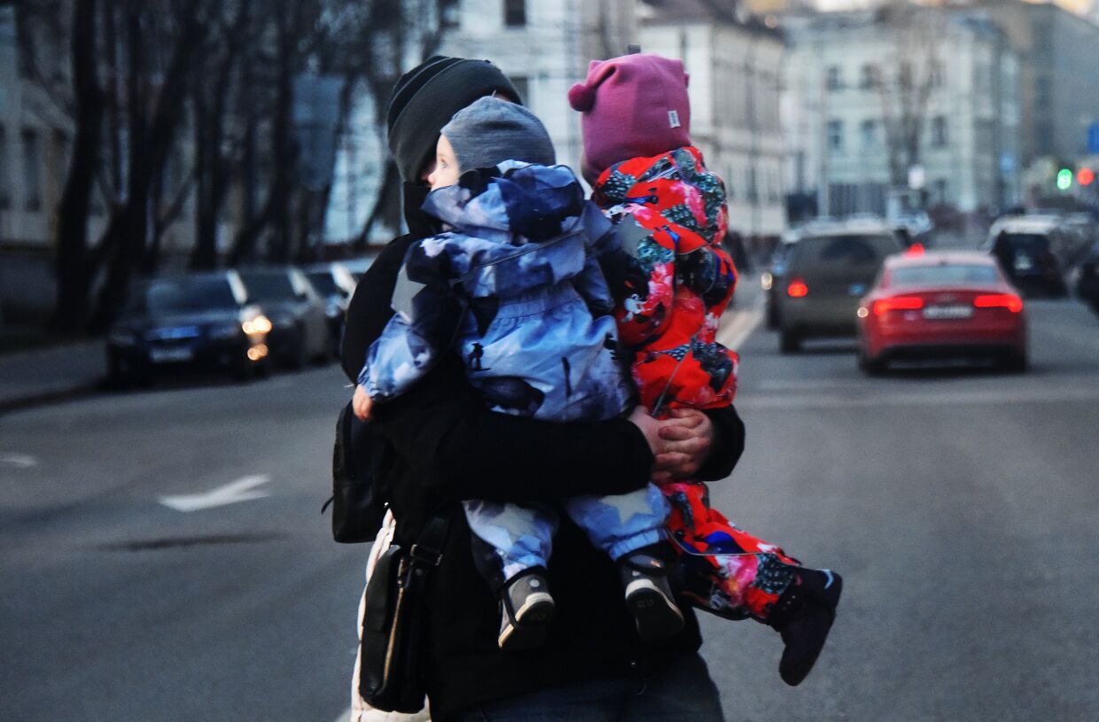 Женщина с двумя детьми на руках переходит дорогу