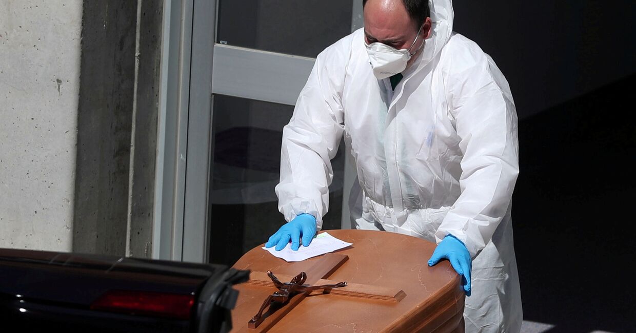 Работник похоронного бюро в защитном костюме перемещает гроб с телом погибшего от коронавируса, Испания