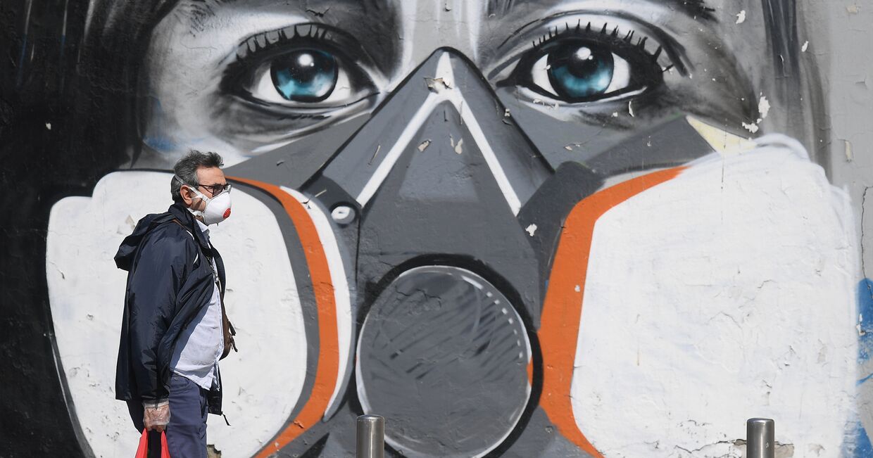 Мужчина в маске идет мимо граффити в Милане, Италия