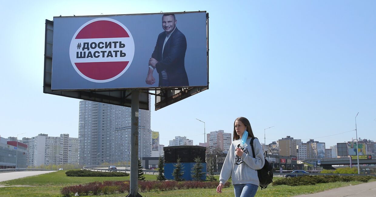 Девушка у рекламного щита, установленного в Киеве в связи с коронавирусом. Надпись: «Хватит шастать»