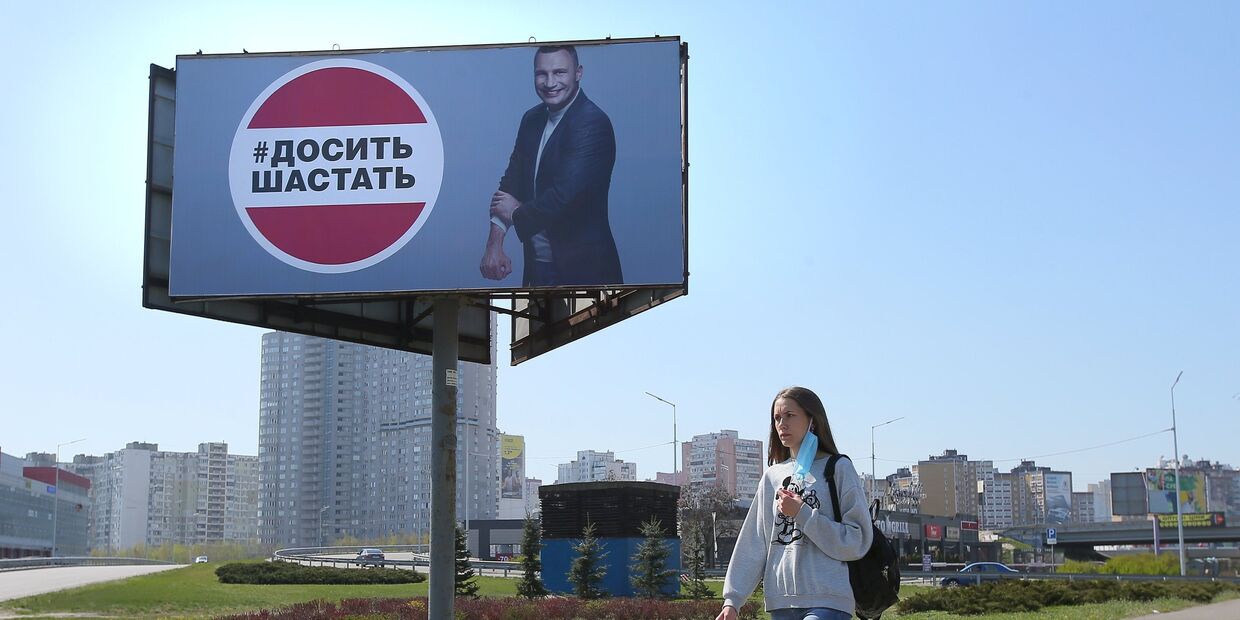 Девушка у рекламного щита, установленного в Киеве в связи с коронавирусом. Надпись: «Хватит шастать»