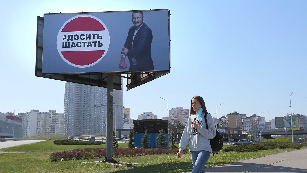 Девушка у рекламного щита, установленного в Киеве в связи с коронавирусом. Надпись: «Хватит шастать»