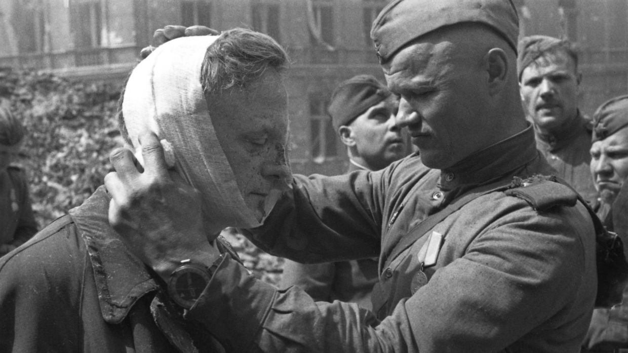 Великая Отечественная война 1941-1945 гг. Взятие Берлина Красной Армией. Советский солдат оказывает медицинскую помощь раненому местному жителю.