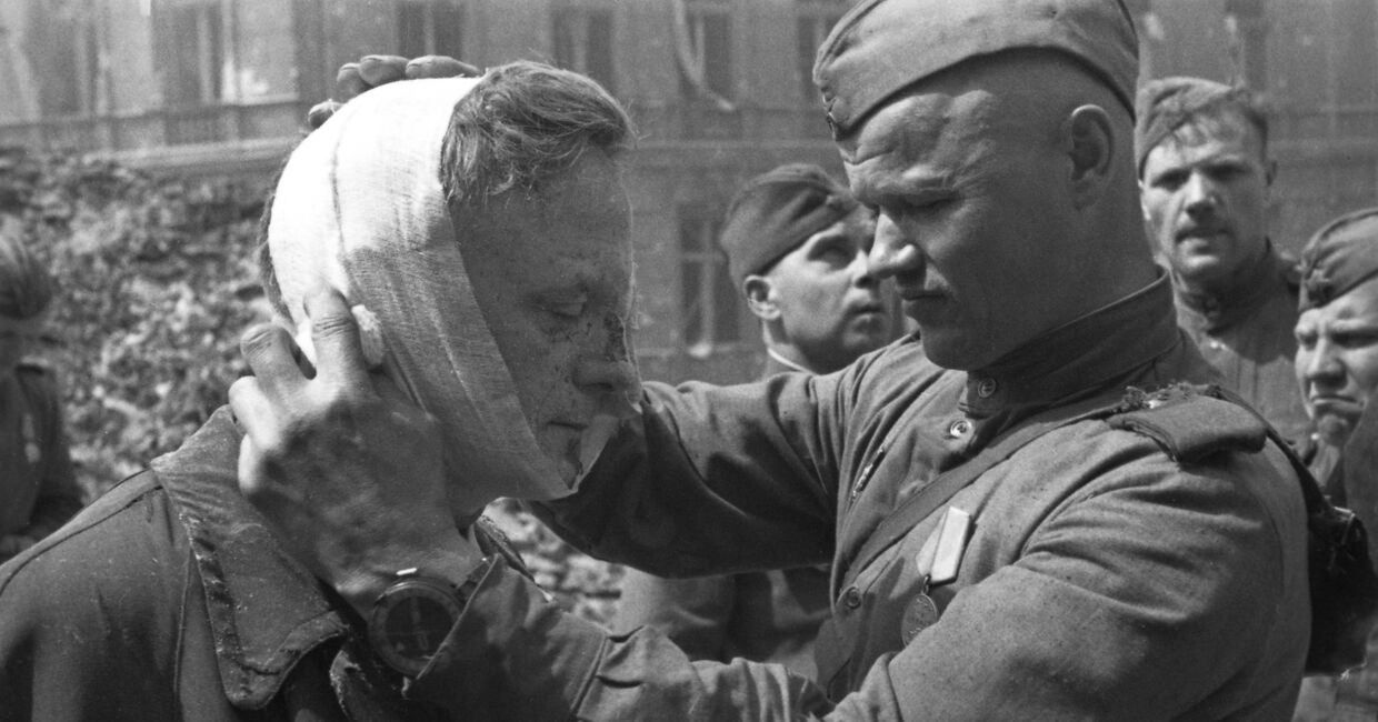 Великая Отечественная война 1941-1945 гг. Взятие Берлина Красной Армией. Советский солдат оказывает медицинскую помощь раненому местному жителю.