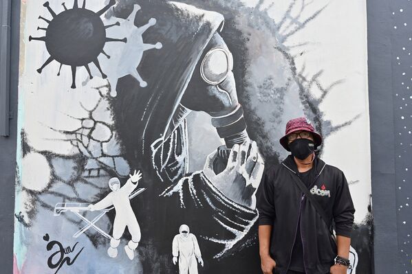 Уличный художник Джунаиди Софьян рядом со своим граффити в Депоке, Индонезия