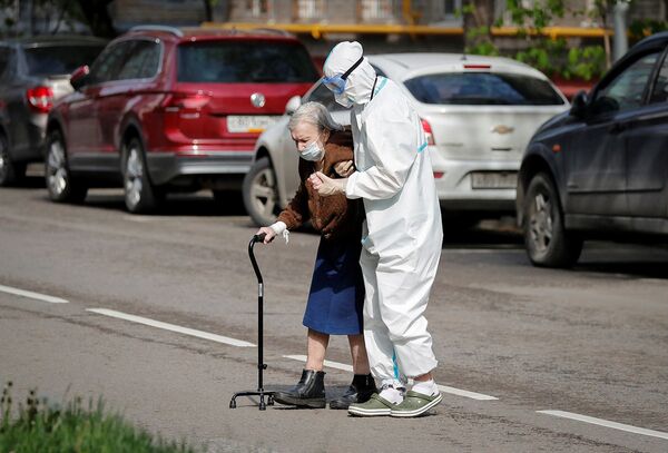 Медицинский работник помогает пожилой женщине перейти дорогу в Москве