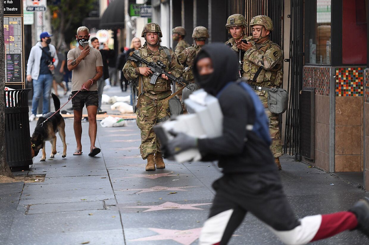 Мародер с коробками пробегает мимо солдат национальной гвардии США в Голливуде