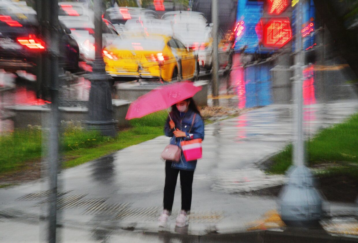 Девушка под зонтом у пешеходного перехода ждет переключения светофора на зеленый свет во время дождя, Москва