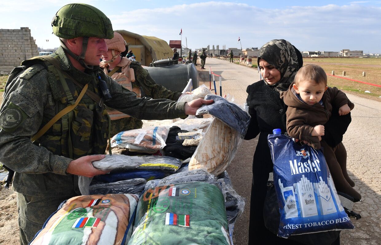 Военнослужащие российского центра по примирению враждующих сторон раздают гуманитарную помощь сирийским беженцам на территории гуманитарного коридора Абу-Духур в окрестностях провинции Идлиб