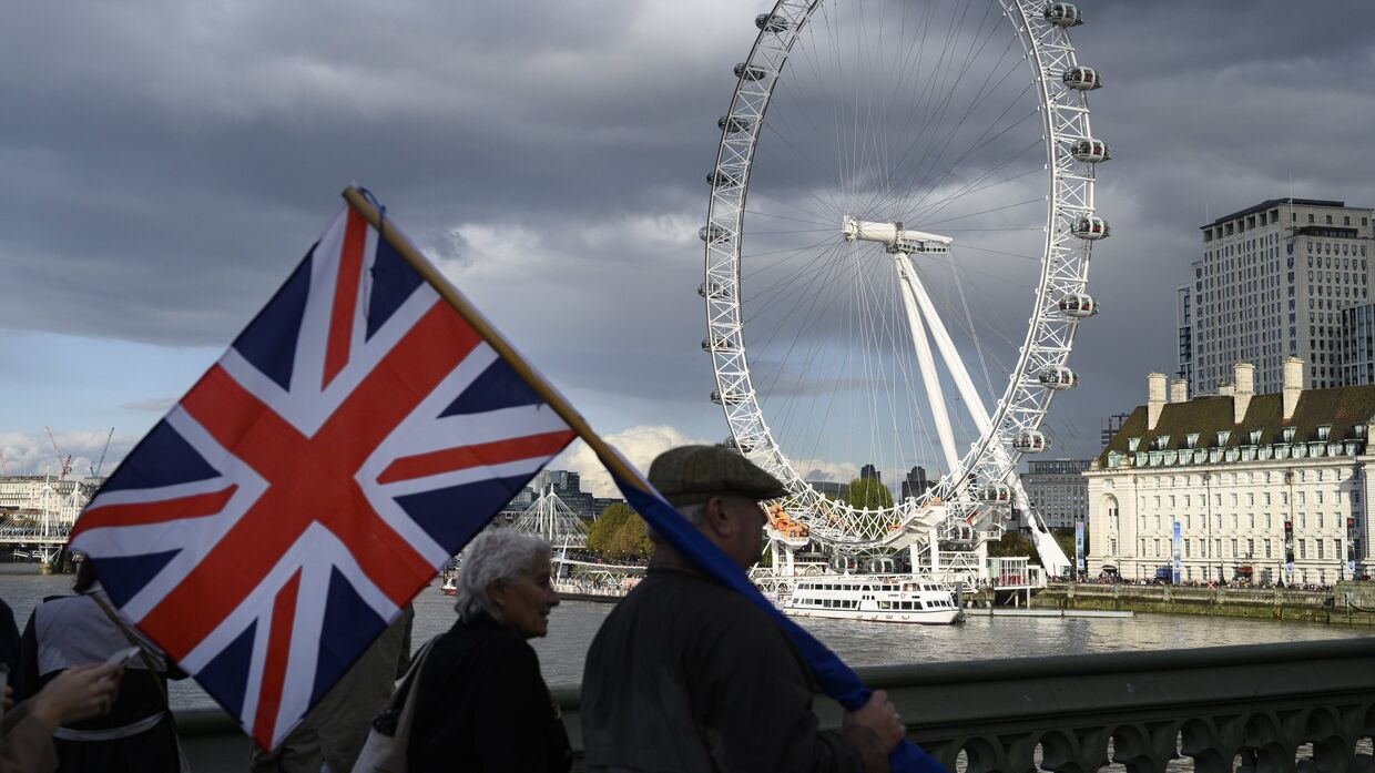 Люди с британским флагом на фоне лондонского колеса обозрения