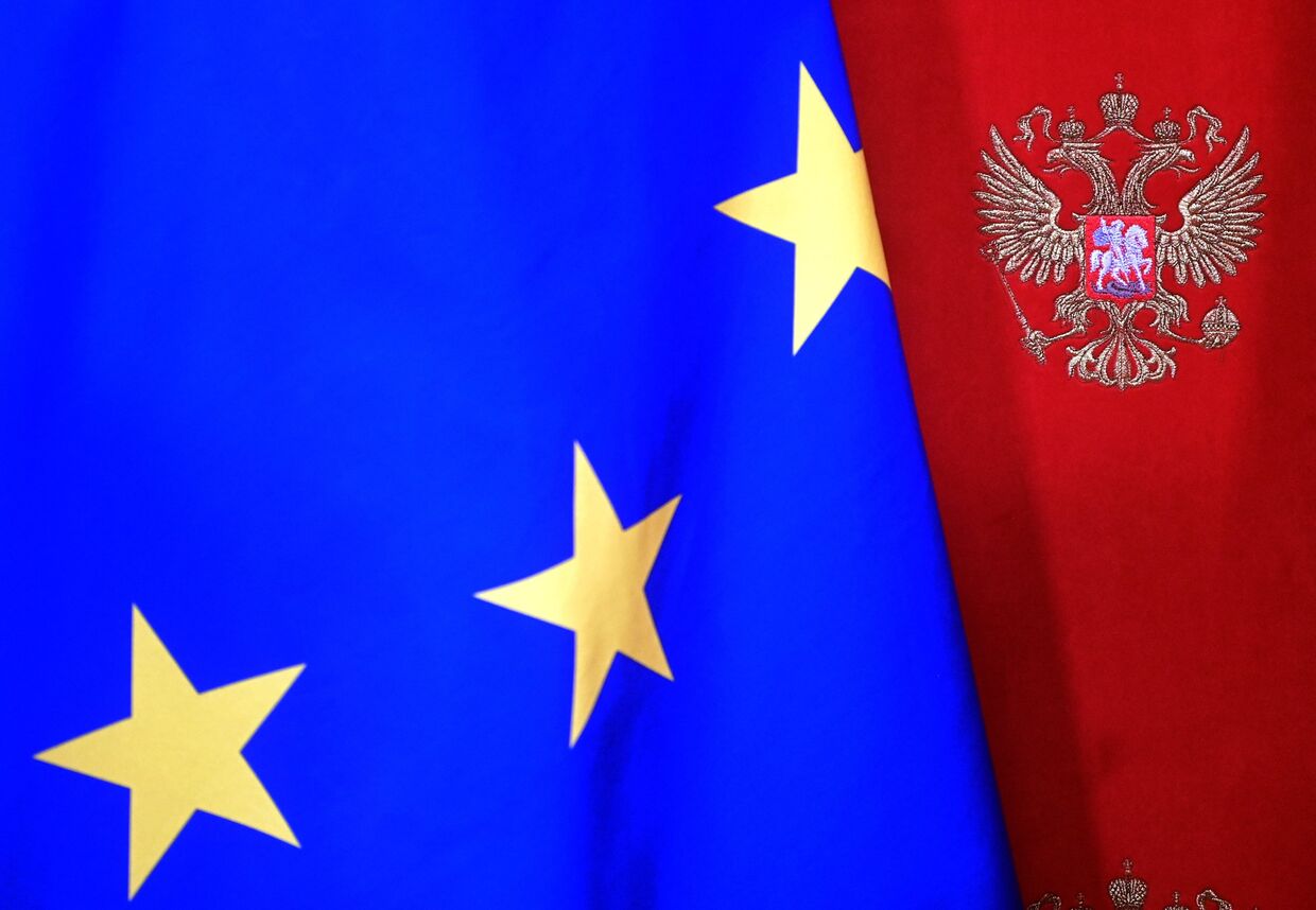 Флаг Евросоюза на фоне стены с гербом РФ