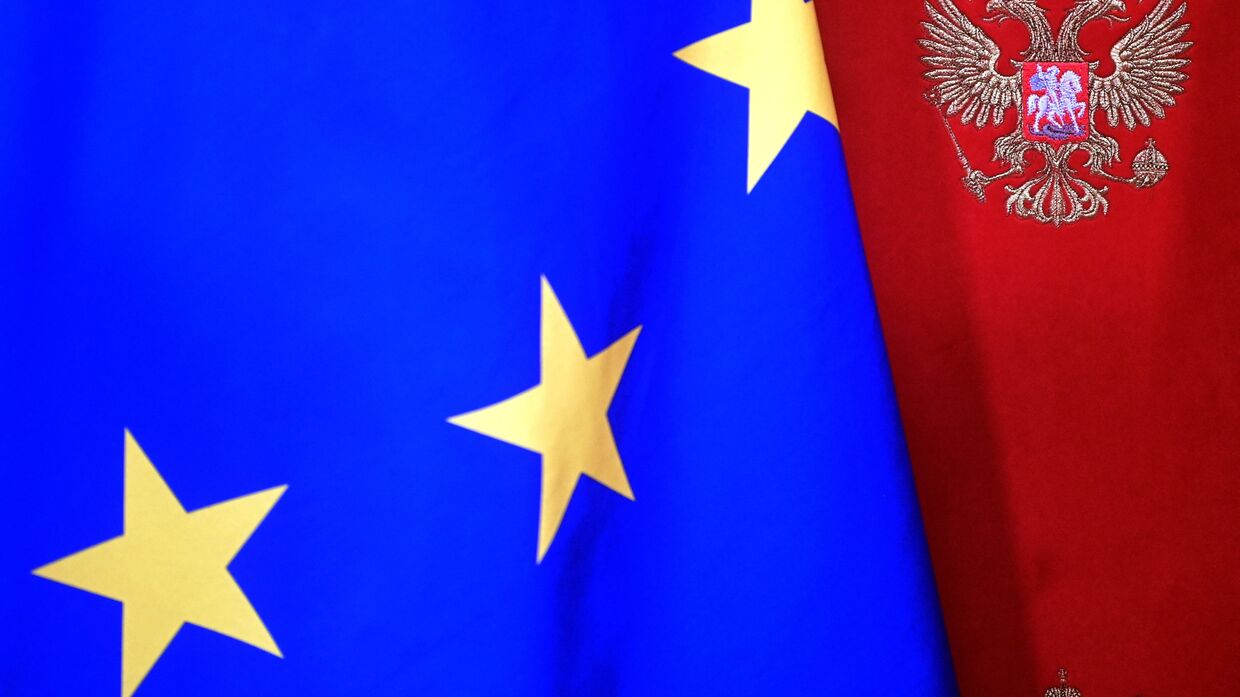 Флаг Евросоюза на фоне стены с гербом РФ
