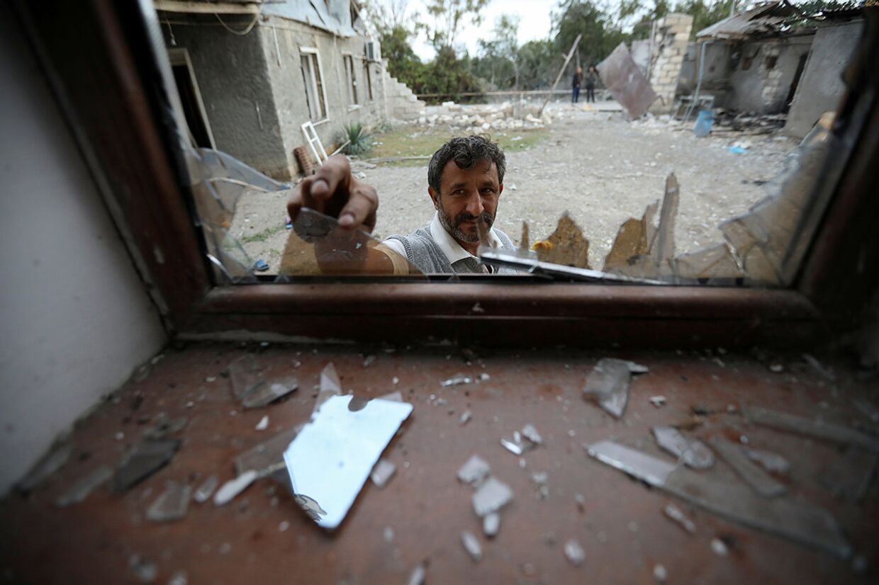 Мужчина убирает битое стекло после обстрела в селе Гарагоюнлу, Азербайджан