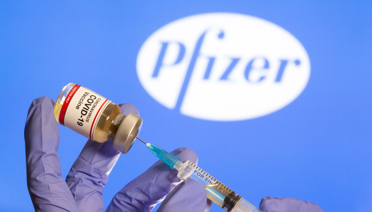 30 октября 2020. Медработник набирает препарат на фоне логотипа Pfizer