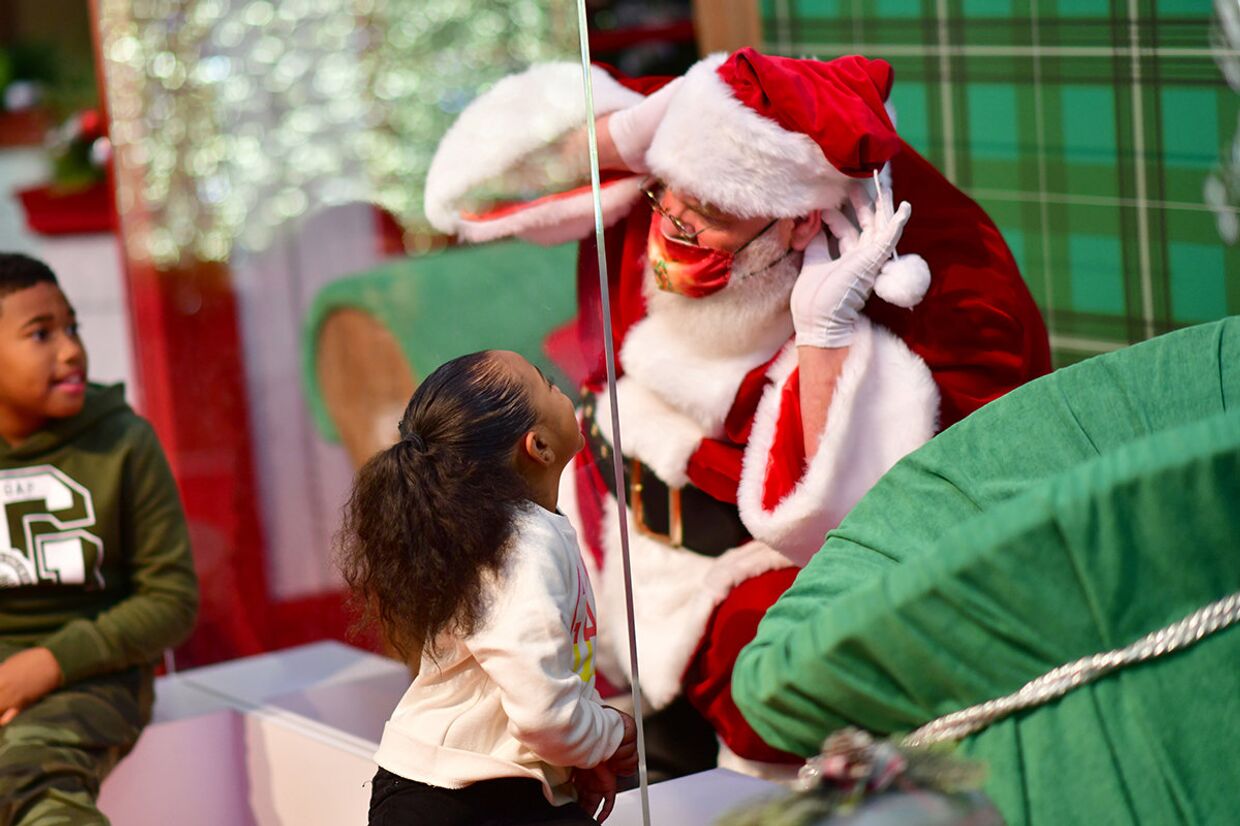 Дети общаются с Санта-Клаусом, сидящим за защитным стеклом