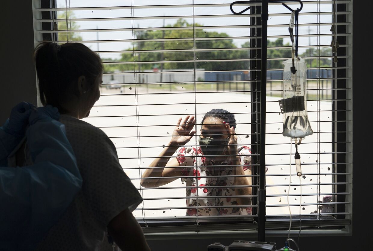 Пациентка общается через стекло с родственниками в госпитале United Memorial Medical Center в Хьюстоне, где проходят лечение больные с covid-19