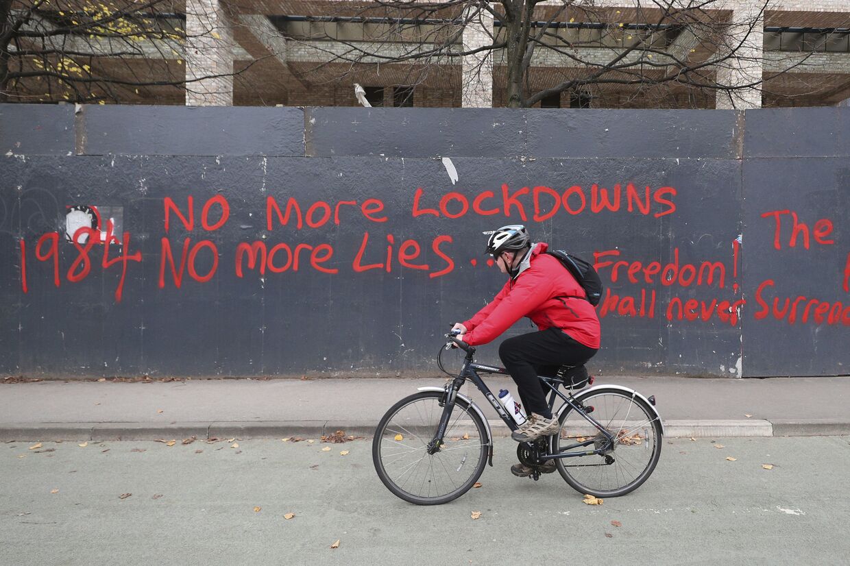 Велосипедист проезжает мимо забора со словами протеста против локдауна в Манчестере, Великобритания