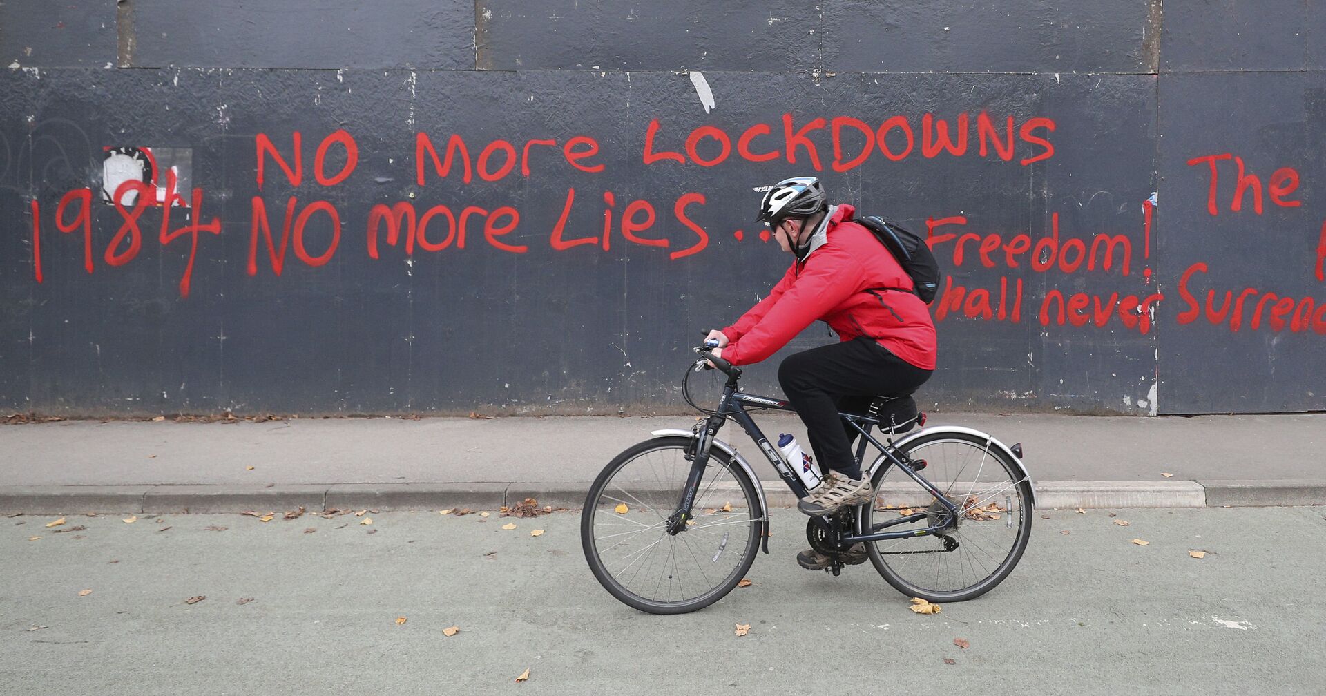 Велосипедист проезжает мимо забора со словами протеста против локдауна в Манчестере, Великобритания - ИноСМИ, 1920, 18.03.2021