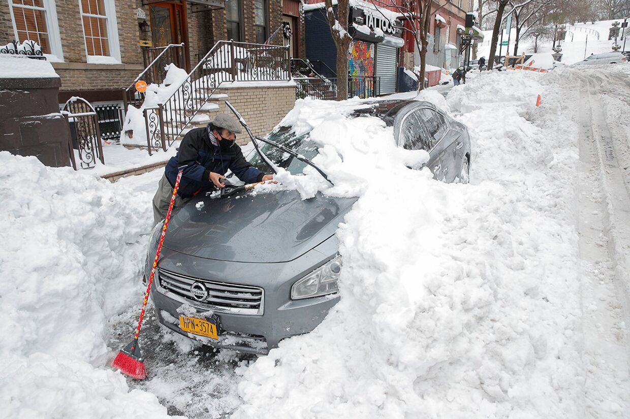 Мужчина отчищает автомобиль от снега в Нью-Йорке
