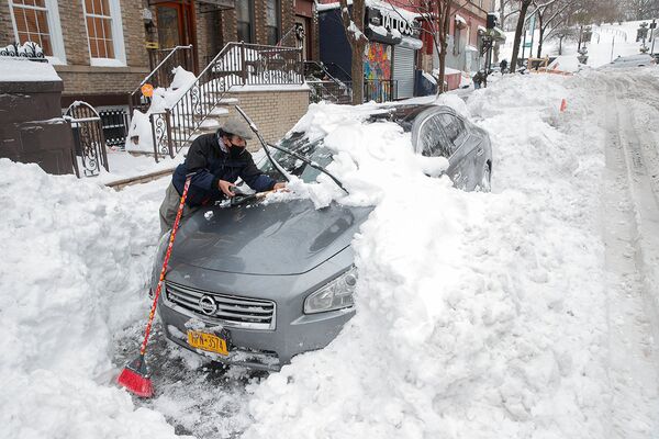 Мужчина очищает автомобиль от снега в Нью-Йорке