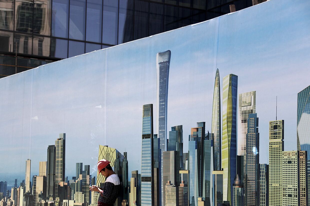 Рабочий у стены строительной площадки с изображением небоскребов в центральном районе Пекина