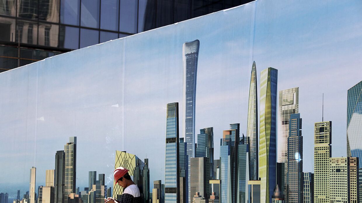 Рабочий у стены строительной площадки с изображением небоскребов в центральном районе Пекина