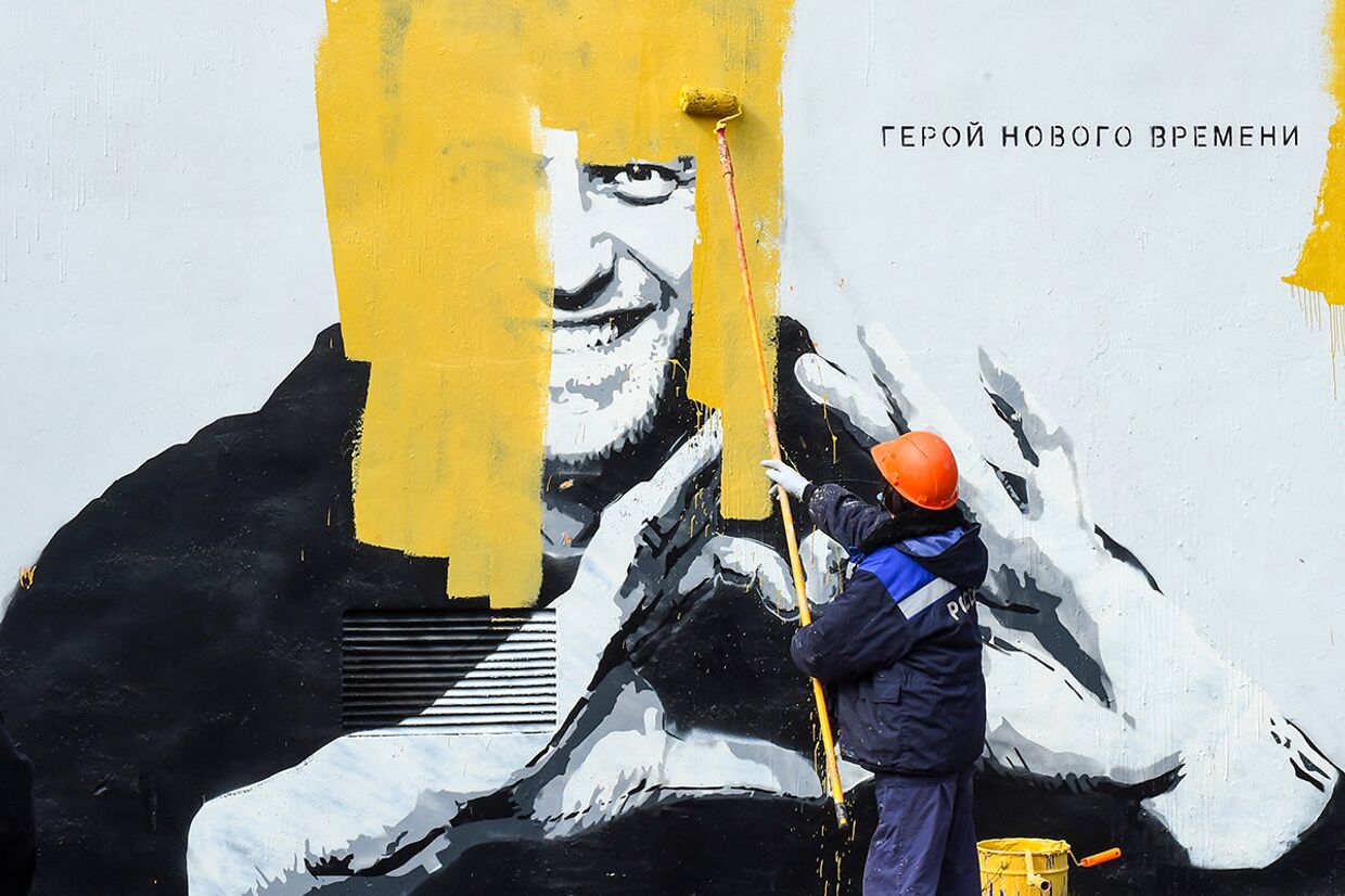 Рабочий закрашивает граффити, изображающее Алексея Навального в Санкт-Петербурге