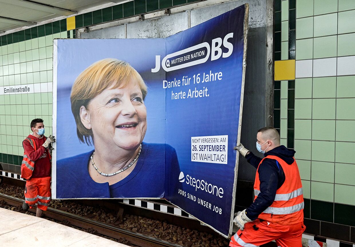 Рабочие снимают плакат с изображением канцлера Германии Ангелы Меркель